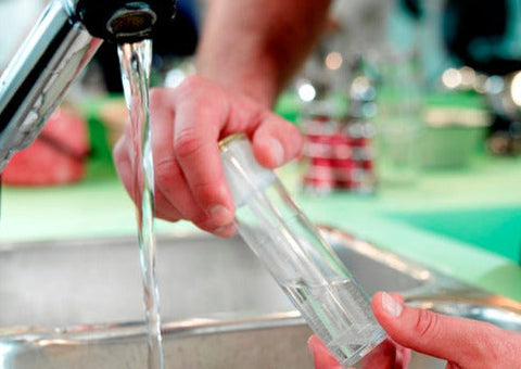 Wasser läuft aus einem Wasserhahn und daneben ein befülltes Probenahmeröhrchen